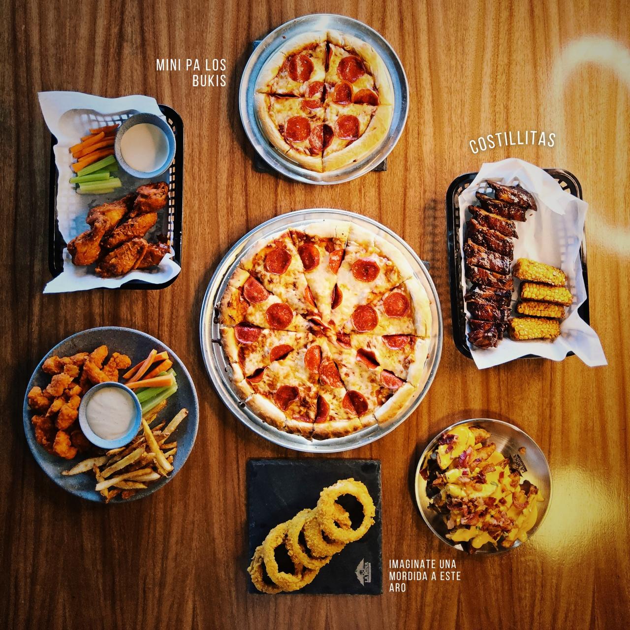 Pizza, costillitas, alitas y entradas sobre mesa de madera